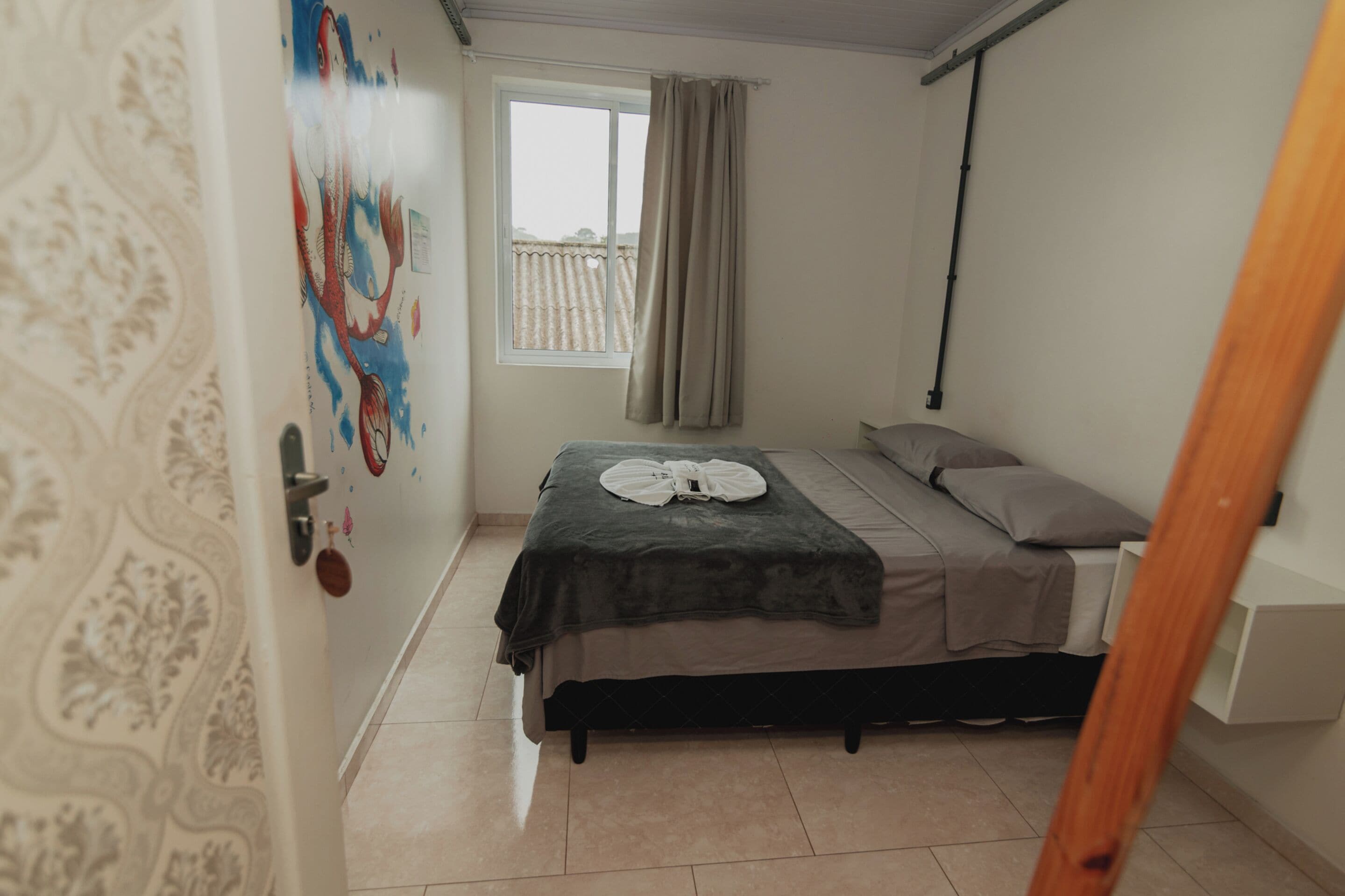 A bedroom with a bed, a window with curtains, a wall with a decorative pattern, and a door.
