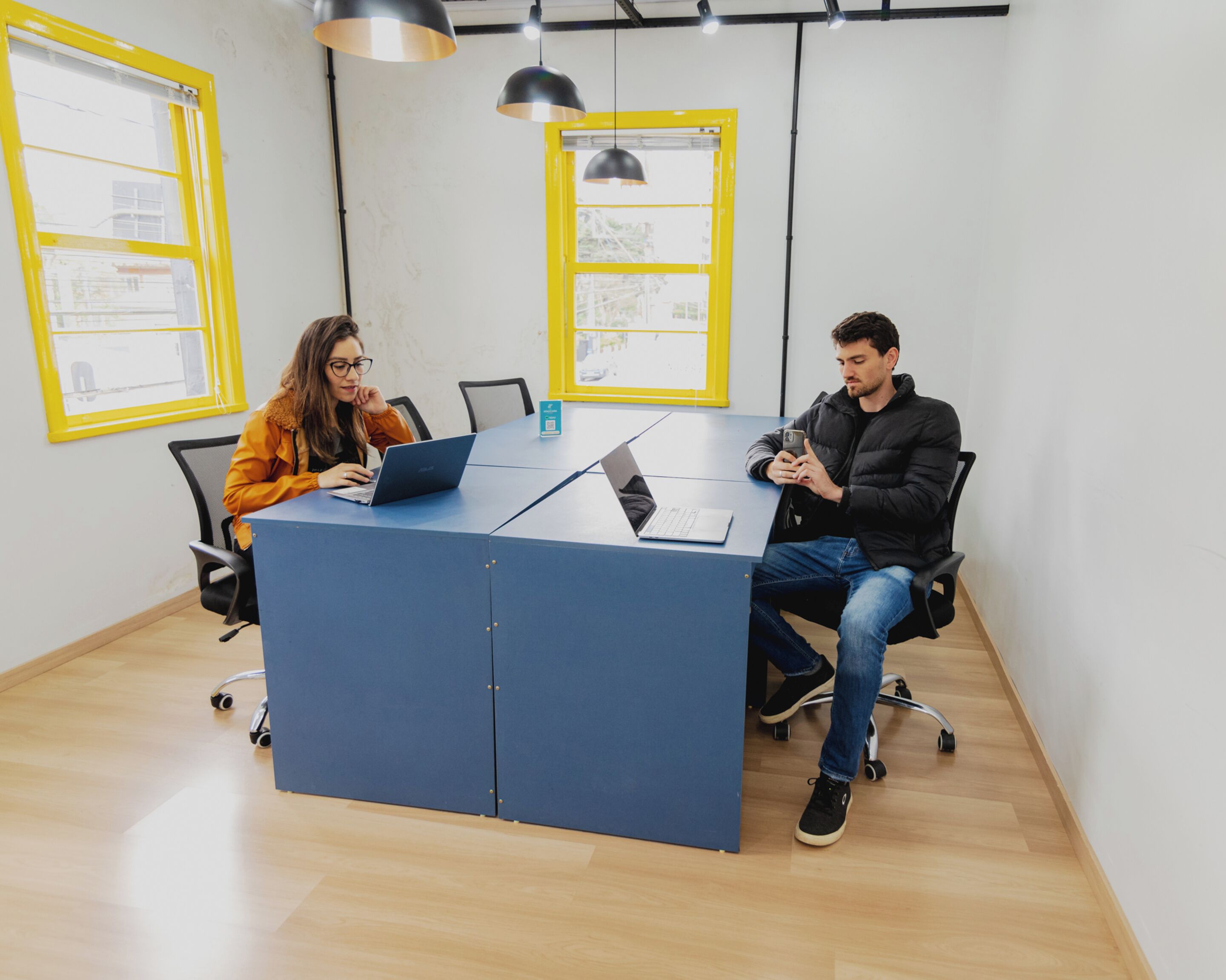 A conference room with a blue table, two laptops, and two people working.