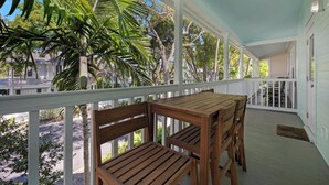 A covered porch with wooden furniture and white railings, surrounded by lush greenery.