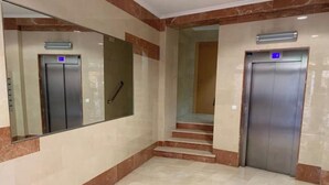 Pasillo con dos ascensores, suelo de mármol y una escalera que sube a otro piso.