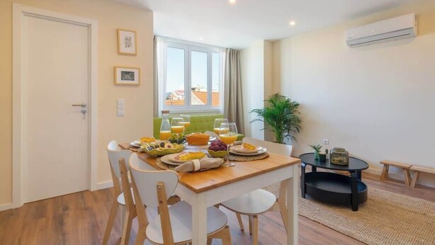 Un comedor con una mesa de madera dispuesta para el desayuno, un sofá verde y una planta en maceta.