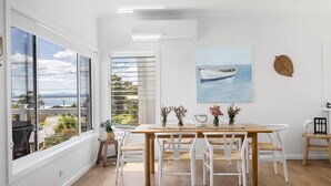 A dining area with a wooden table, white chairs, and a view of the sea through large windows.