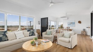 A spacious living room with a large window, a round wooden coffee table, and a dining area with a view of the outdoors.