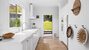 A modern kitchen with white cabinetry, a large window, and a view of a garden.