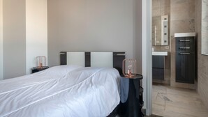 Ein modernes Hotelzimmer mit einem großen Bett, Nachttischen, einem Badezimmer mit Spiegel und Waschbecken sowie einer Duschkabine.