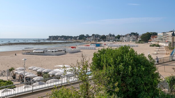 Ein Hotel am Strand mit Außenbereich, Blick auf das Meer und Gebäuden im Hintergrund.