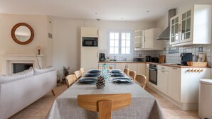 Une cuisine moderne avec des meubles blancs, une table à manger pour quatre personnes et un four encastré.