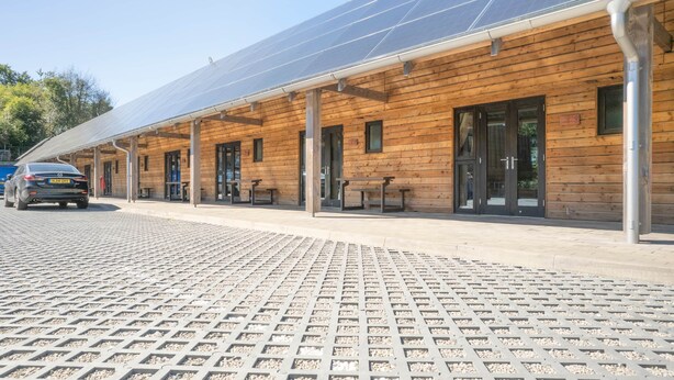 A wooden building with solar panels on the roof, outdoor seating, and a paved area. - Elm - Flimwell Park Lodges (Ticehurst)