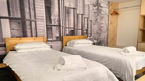Two single beds with white linens and towels, wooden headboards, and a large window with a view of trees and buildings. - Elm - Flimwell Park Lodges (Ticehurst)