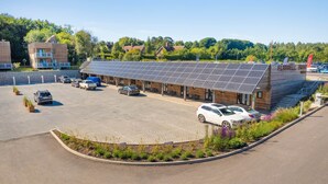 Een modern gebouw met een dakbedekt met zonnepanelen, een parkeerplaats en een kleine tuin.