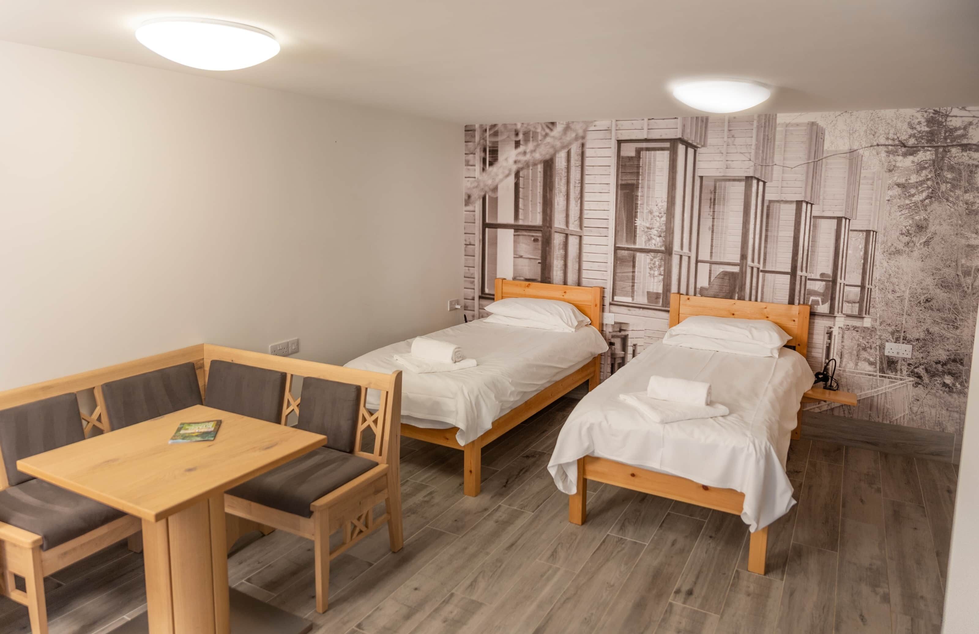 Una habitación con dos camas de madera, una mesa de madera con sillas y un mural en la pared.