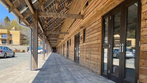 A covered wooden walkway leading to a building with large glass doors. - Birch - Flimwell Park Lodges (Ticehurst)