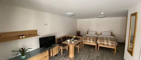 A compact room with a bed, a desk, a TV, and a small plant.