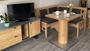 Un soggiorno moderno con un tavolo da pranzo in legno, sedie imbottite, un televisore a schermo piatto su un mobile in legno e una pianta in vaso.