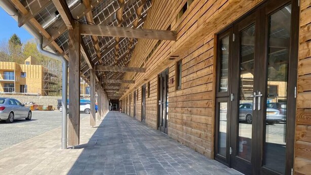 Una passerella in legno coperta che conduce a un edificio con ampie porte in vetro.