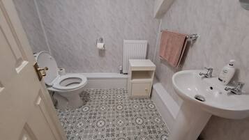 Une salle de bain comprenant des toilettes, un lavabo, une baignoire et un petit meuble de rangement.