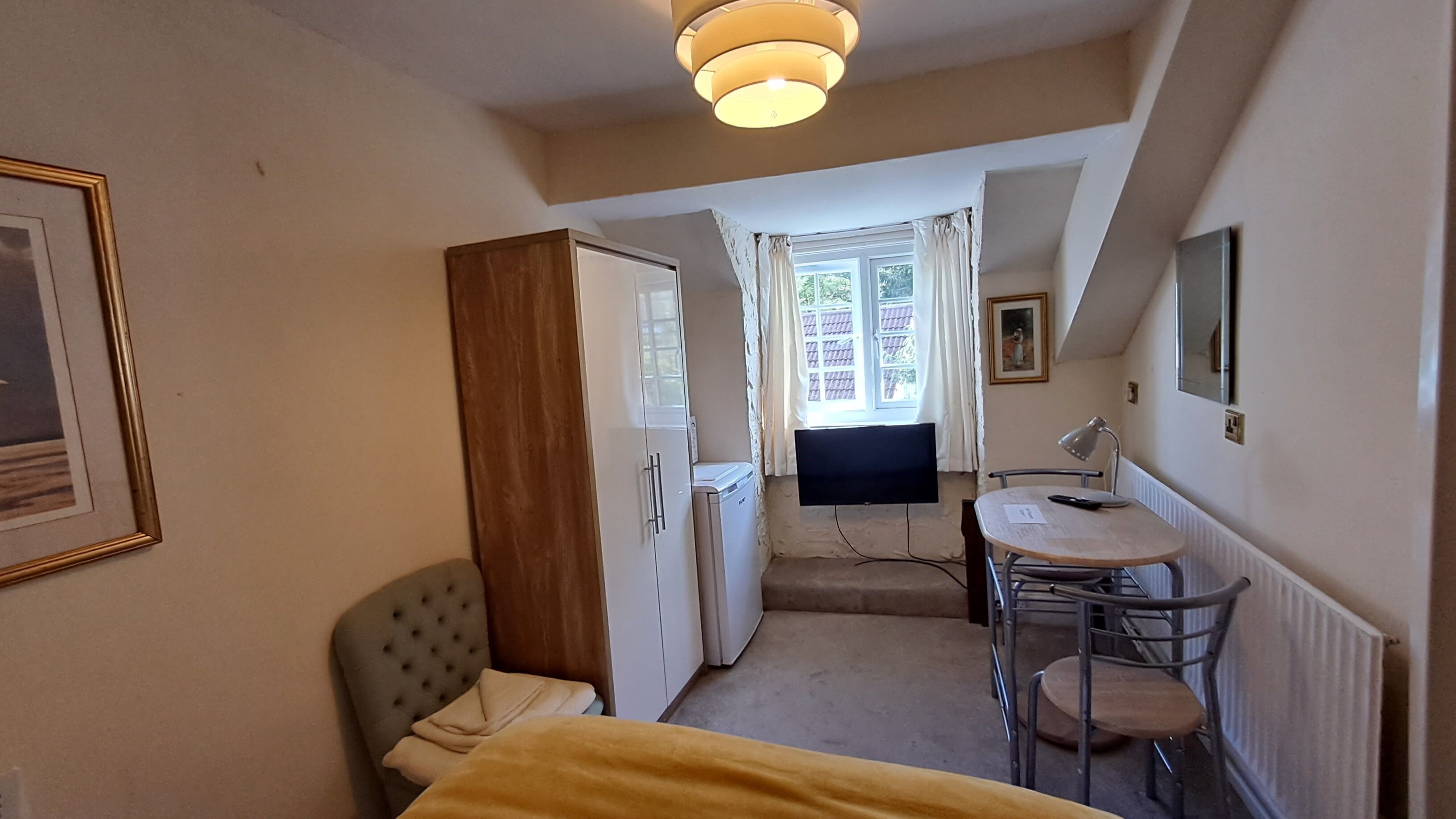 Une petite pièce, de taille modeste, comprenant un lit, un bureau, une chaise, un téléviseur et un radiateur.