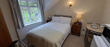 A bedroom with a bed, bedside table, lamp, and a desk with a chair.
