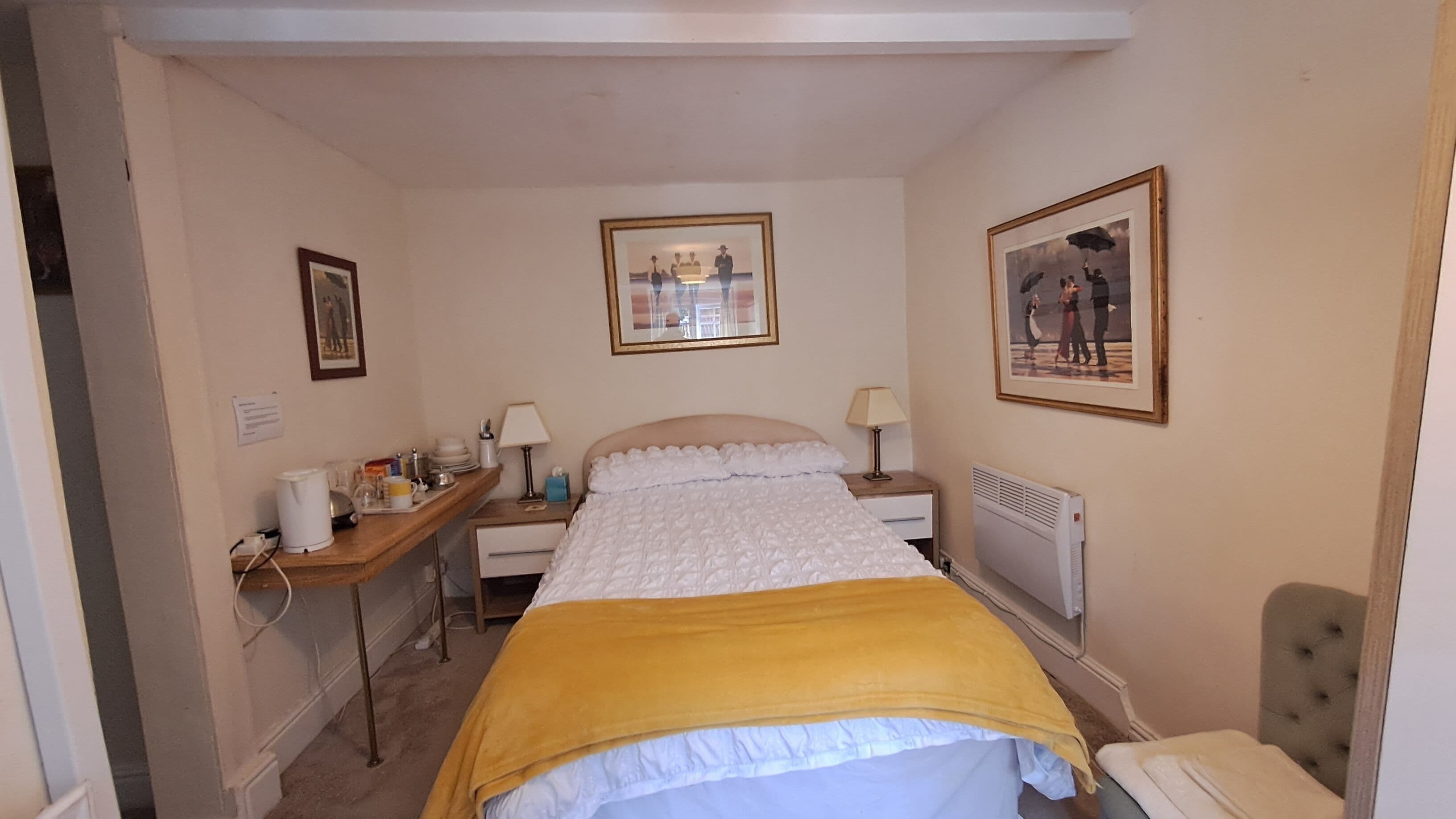 A hotel room with a bed, bedside tables, a desk, a chair, and two framed pictures on the walls.