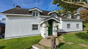 Une maison blanche à deux étages, avec une porte verte, des marches en pierre et des jardinières suspendues.