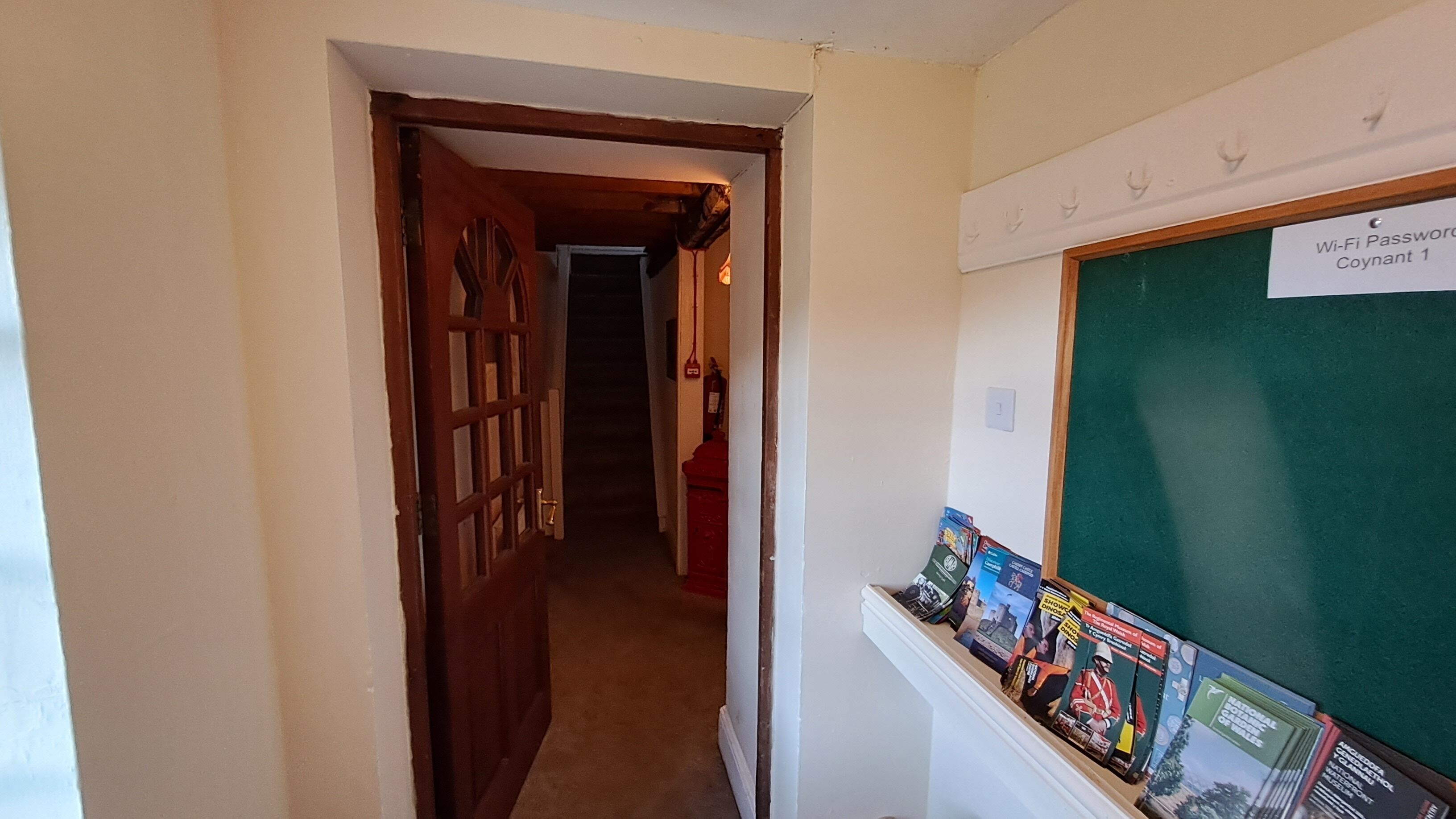 A hallway with a wooden door, a fire extinguisher, and a bulletin board with magazines.