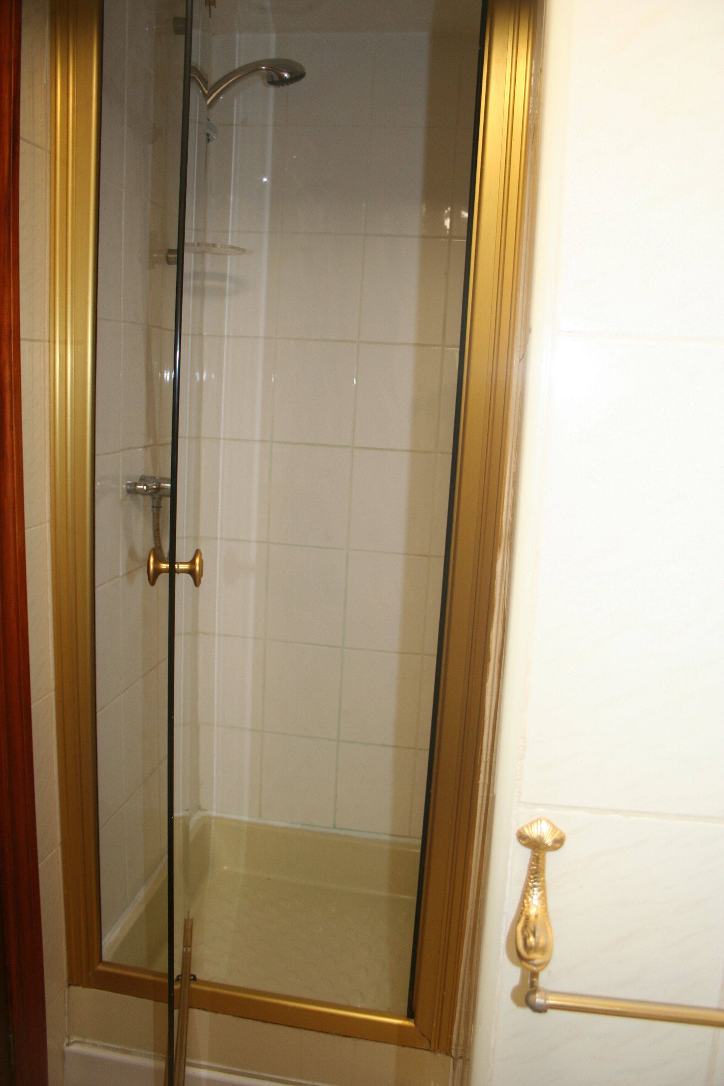 A glass-enclosed shower with a gold frame, white tiled walls, and a gold towel rack.