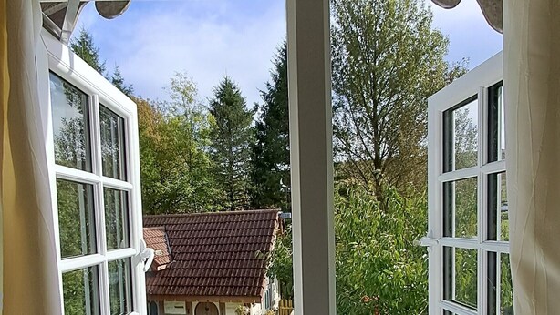 Une pièce dotée d’une grande fenêtre donnant sur un jardin, un petit bâtiment et une cabine téléphonique rouge.
