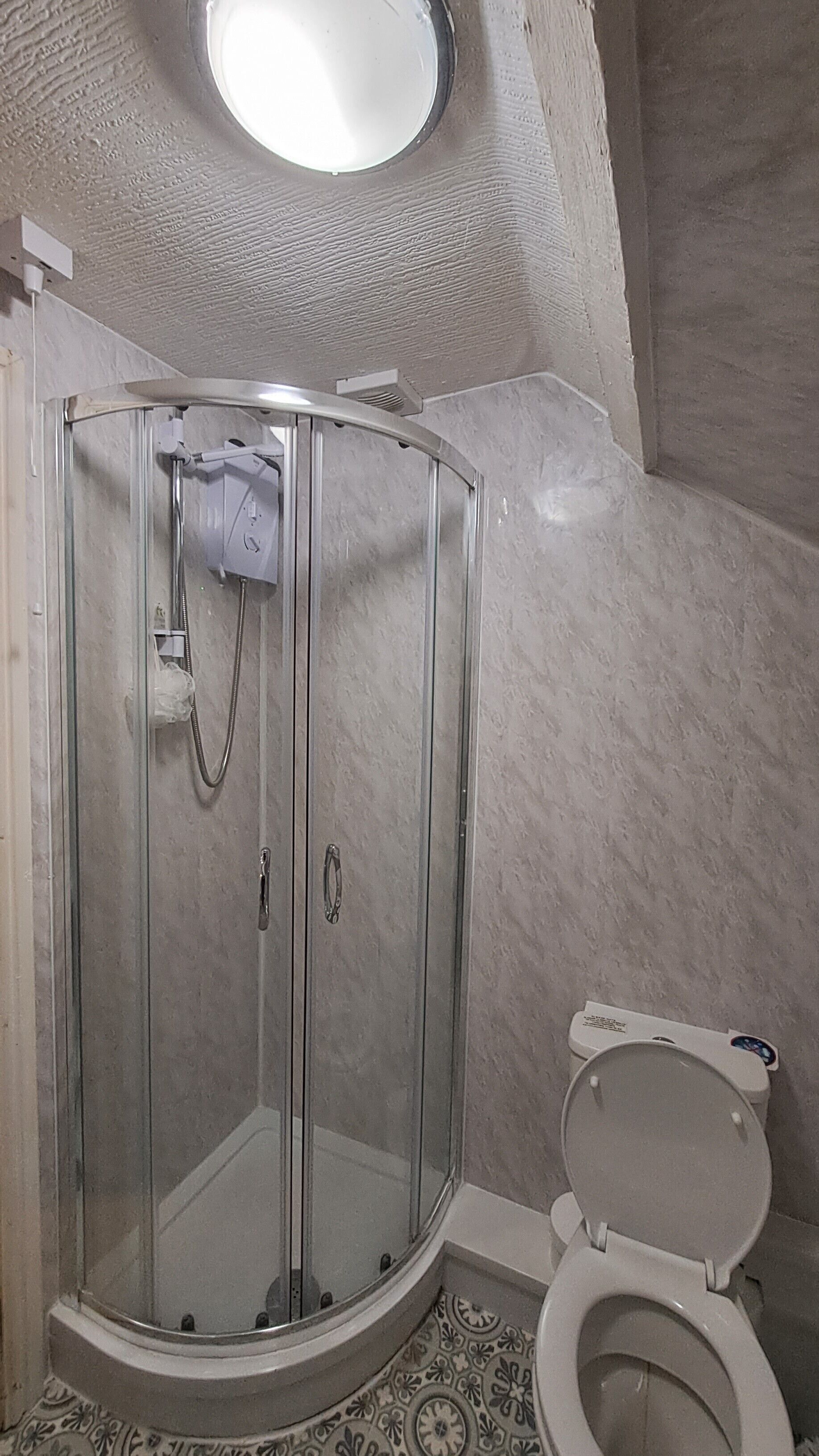 Un baño con ducha de vidrio, inodoro y una ventana pequeña.