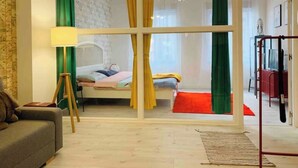 Una habitación con cama, lámpara de pie, sofá y un amplio ventanal con cortinas.