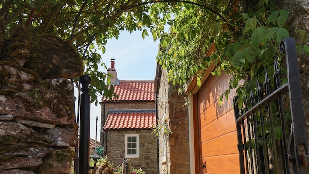 A stone building with a red-tiled roof, a wooden door, and a metal gate. - Bute Cottage (Pickering)