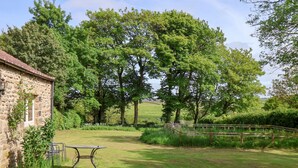 A stone building with a table and chairs in a grassy area with trees and a wooden fence. - Bute Cottage (Pickering)