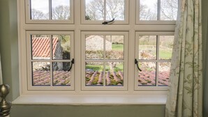 A window with six panes, a curtain, and a view of a garden and buildings. - Bute Cottage (Pickering)