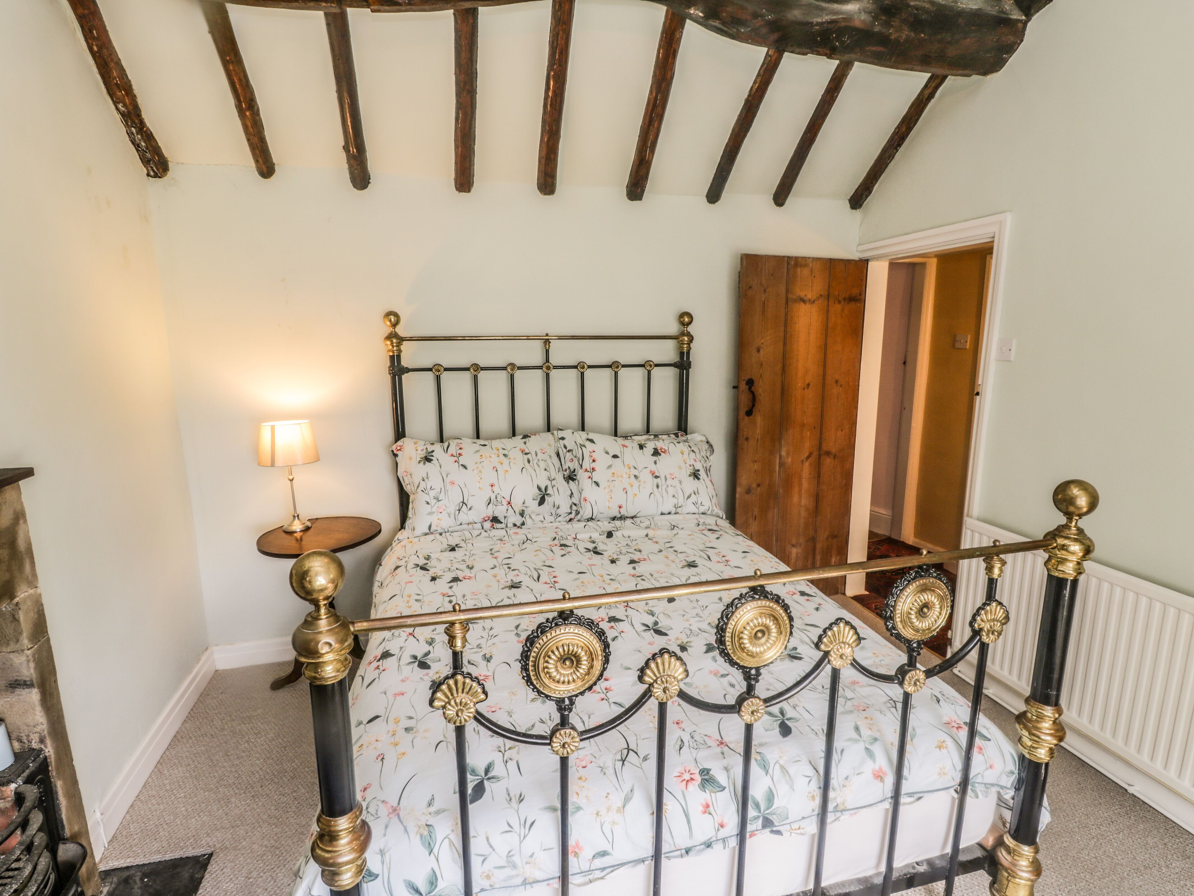 A bed with a floral bedspread, a nightstand with a lamp, and a wooden wardrobe.
