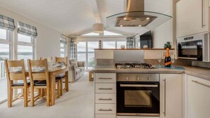 A modern kitchen with a gas stove, oven, and microwave, a dining area with a table and chairs, and large windows offering a view.