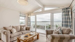 A modern living room with a sofa, armchair, and coffee table, large windows with a view of the sea, and a ceiling with skylights.