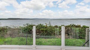 A view of a lake with a fence in the foreground and a clear sky.