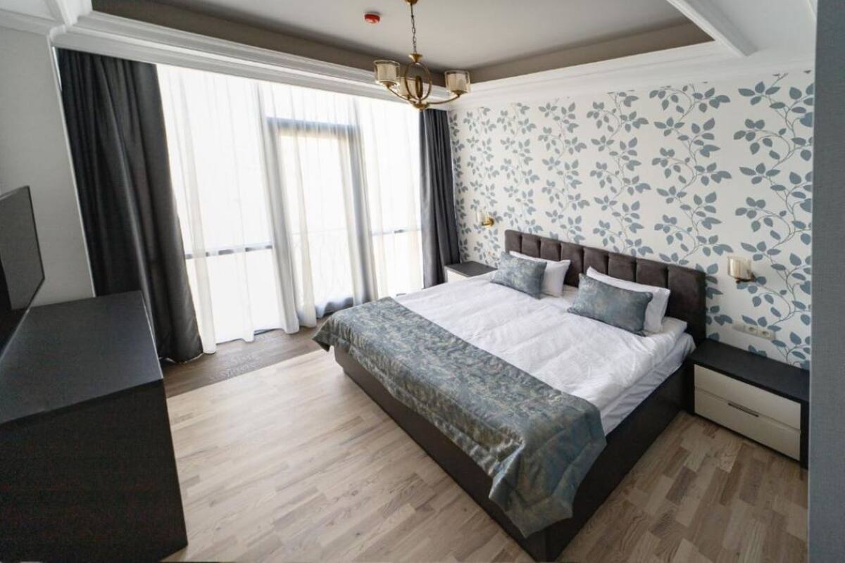 Ein Schlafzimmer mit einem großen Bett, einem Nachttisch, einer Kommode und einem Fenster mit Vorhängen.