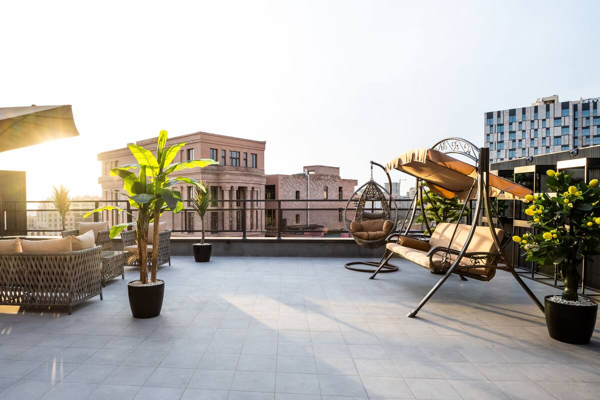 Eine Dachterrasse mit Korbmöbeln, Blumentöpfen und einem Hängesessel.