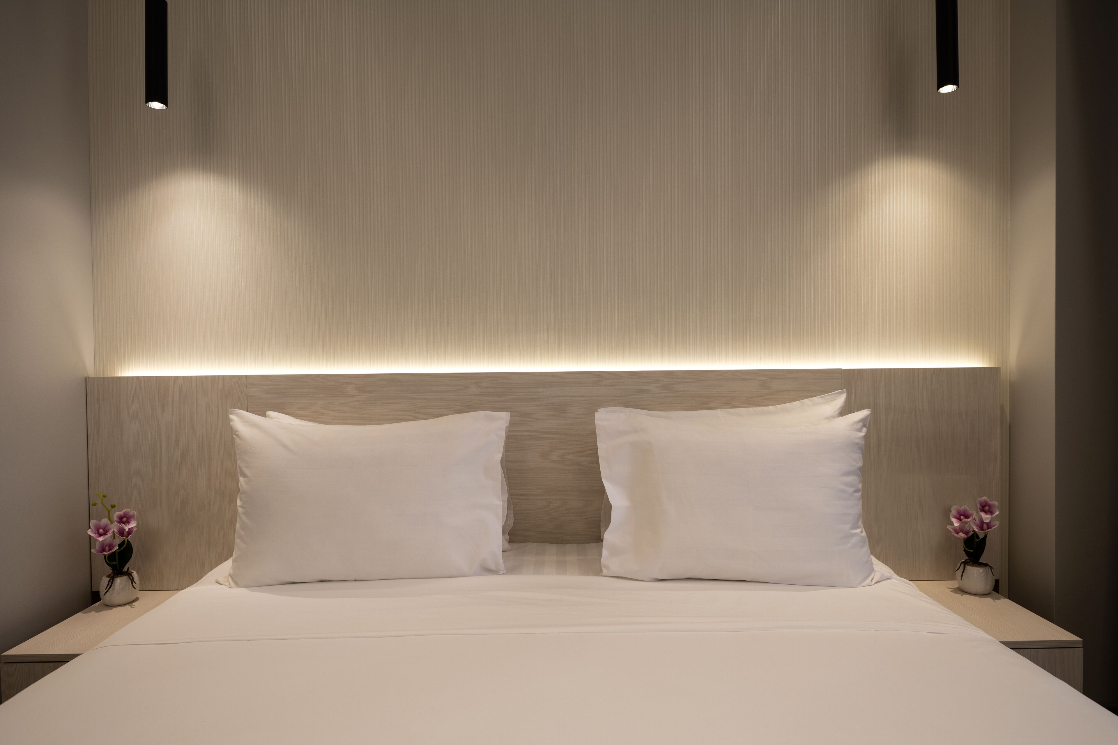 Una camera da letto moderna con un letto grande, due cuscini bianchi e un comodino con un vaso di fiori.