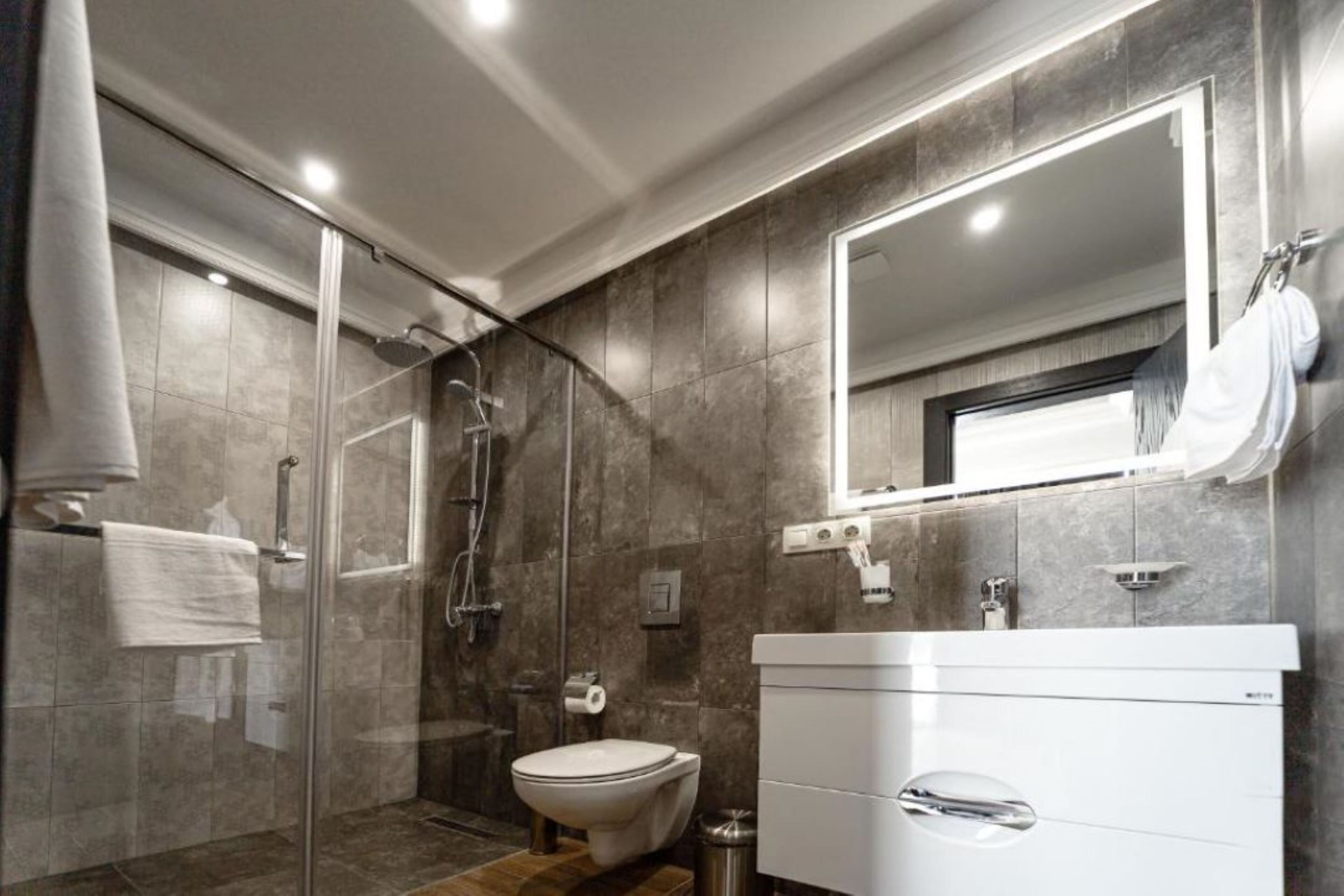 A modern bathroom with a glass shower enclosure, a toilet, and a white vanity with a mirror.
