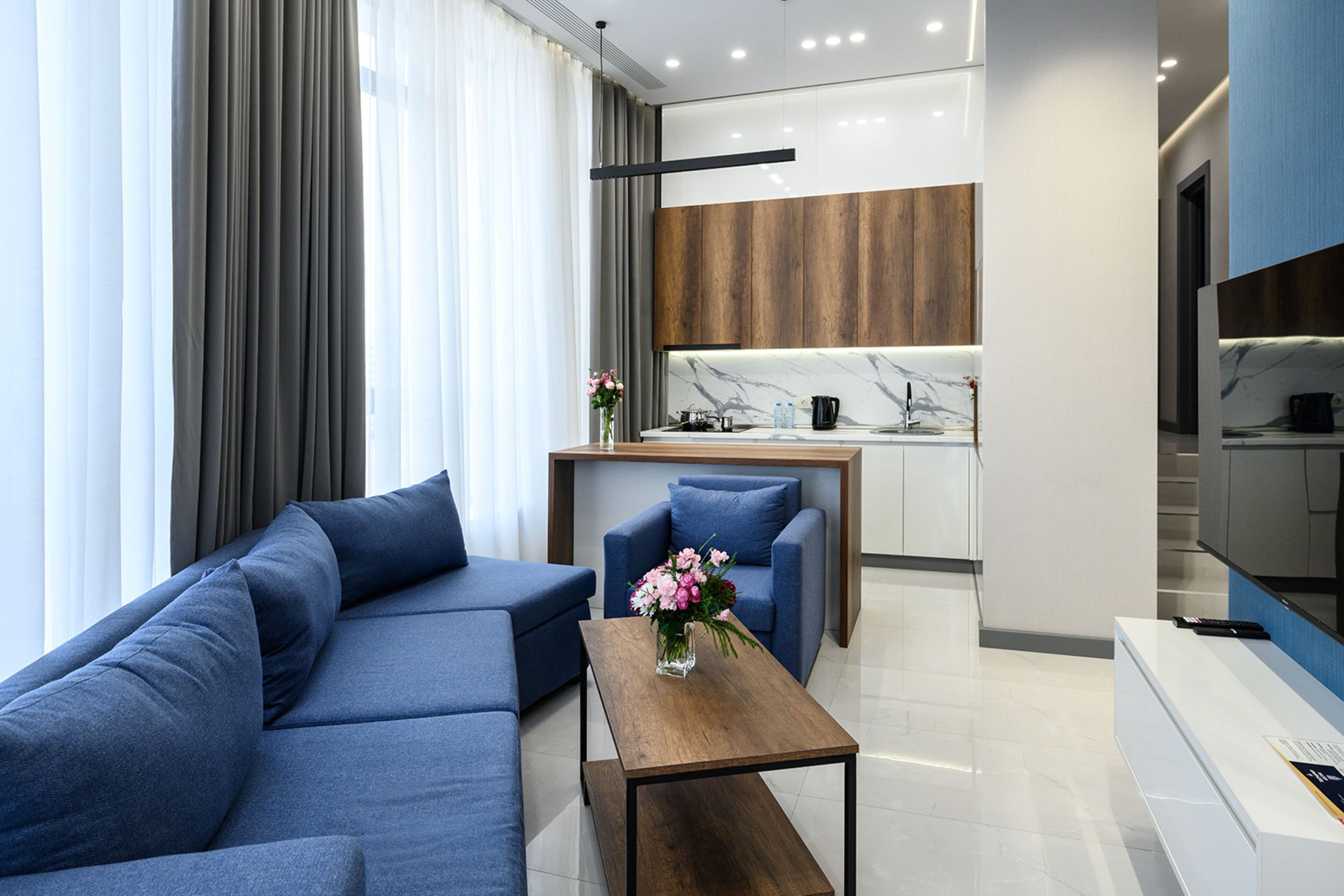 Un salón moderno con un sofá azul, una mesa de centro de madera y una mesita auxiliar con un jarrón de flores.