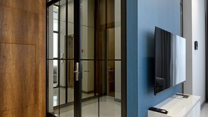 Un interior moderno con un panel de madera en la pared, una puerta de cristal y un televisor montado sobre una consola blanca.