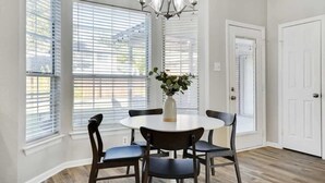 A dining area with a round table and six chairs, large windows with blinds, a chandelier, and a white door. - Lewisville Estate - Spacious 5BR w/ Game Room (Lewisville)