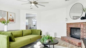 A modern living room with a green sofa, a round coffee table, a fireplace, and a ceiling fan. - Lewisville Estate - Spacious 5BR w/ Game Room (Lewisville)