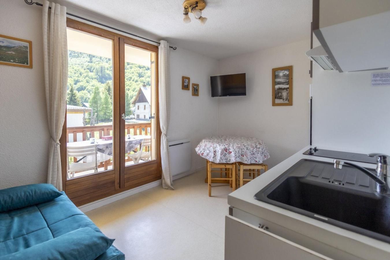 Une pièce comprenant un lit, une table recouverte d’une nappe, un téléviseur et un coin cuisine avec un évier.