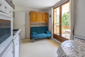 A bedroom with a bed, a blue sofa, a wooden wardrobe, and a sliding glass door leading to a balcony.