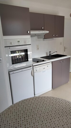A compact kitchen with a built-in oven, microwave, and dishwasher, featuring grey cabinets and a patterned tablecloth.