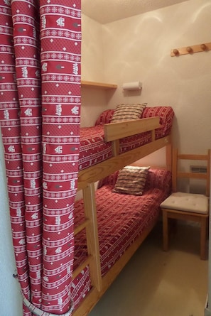 A bunk bed with red bedding and a wooden headboard. A small wooden chair is beside the bed. - 1st floor, parking, 26m², Valloire (Valloire)