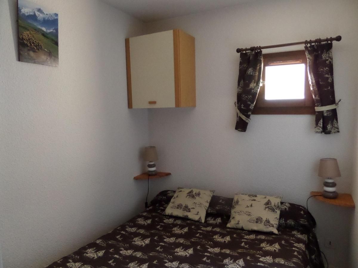 A bedroom with a bed, a wardrobe, a window with curtains, and a lamp on a bedside table.