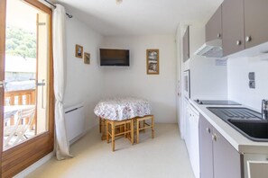 Eine kleine Küche mit Esstisch, Fernseher und Blick ins Freie.